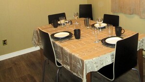 Comedor con una mesa dispuesta para cuatro, sillas, un cuadro en la pared y una ventana con cortinas.