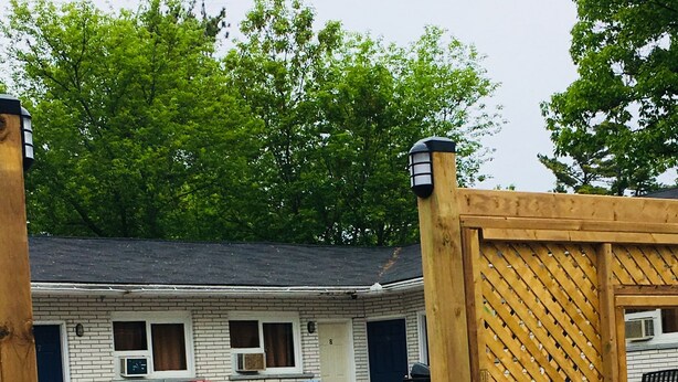 Un motel con área de estar al aire libre, que incluye sillas Adirondack rojas y azules, y una valla de madera.