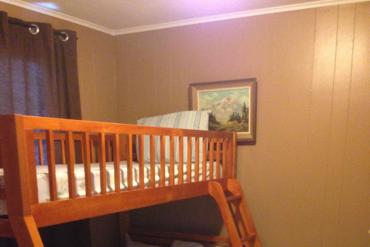 A bunk bed with a wooden frame and white bedding in a room with wooden flooring and a painting on the wall.