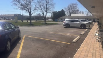 Un estacionamiento con varios automóviles, un edificio de motel y un sendero de ladrillo que conduce a una fila de mesas y sillas.