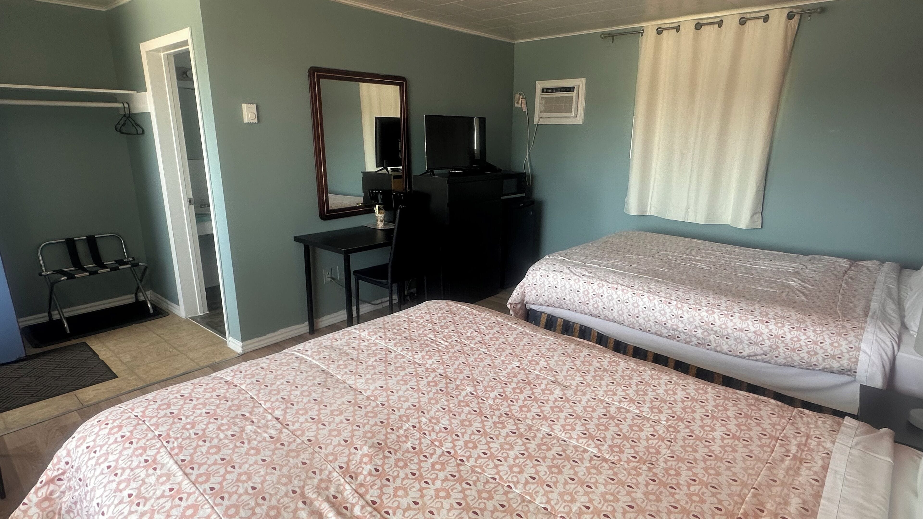 A bedroom with a bed, a desk, a chair, a mirror, and a television.