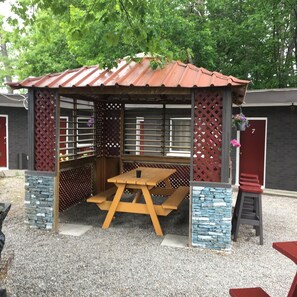 A covered outdoor seating area with a picnic table, a small stool, and a bench. - Edgewater Resorts - Edgewater Inn (Wasaga Beach)