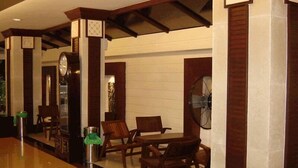 A lobby with wooden furniture, a clock, and a fan. - Rambuttri House (Bangkok)