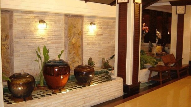 A lobby with a checkered floor, a stone wall with a mural, and three large decorative vases with plants. - Rambuttri House (Bangkok)