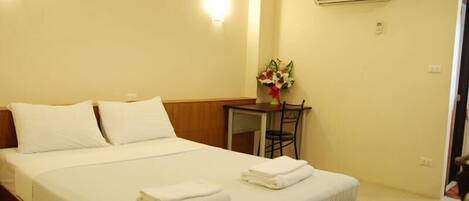 A hotel room with a bed, a small table with a chair, and an air conditioning unit on the wall.