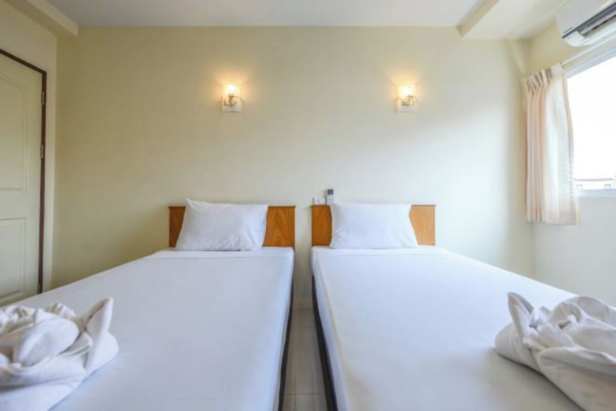 A hotel room with two single beds, a door, and a window with curtains.