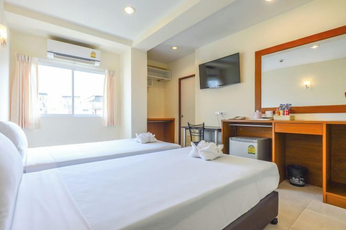 Quarto de hotel com duas camas, uma escrivaninha, uma cadeira, uma televisão e ar condicionado.