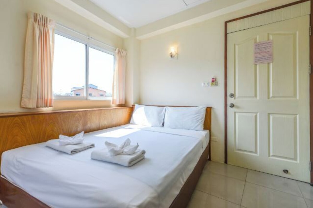 A hotel room with a bed, a window with curtains, a door, and a wall-mounted light.