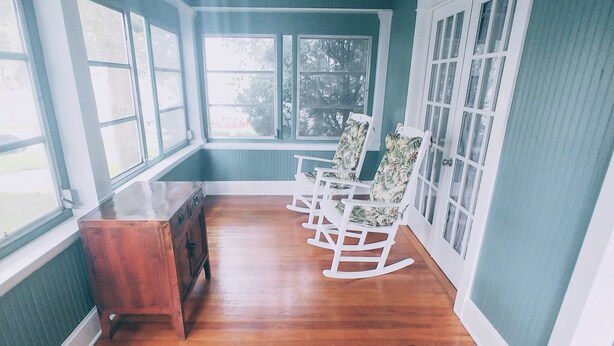 Une pièce avec un plancher en bois, un fauteuil à bascule, une commode en bois et une fenêtre donnant sur des arbres.