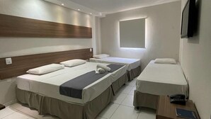 A hotel room with three beds, a wooden headboard, a window, a TV, and a desk with a phone and a notepad. - Hotel Pousada Alagoana (Maceió)