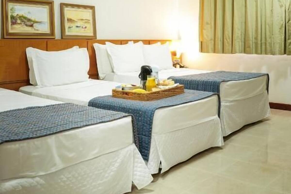 A hotel room with two beds, a wooden headboard, a nightstand with a lamp, and a window with curtains.