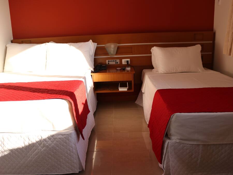 Ett hotellrum med två separata sängar, var och en med ett rött och vitt sängöverkast, ett träbord vid sängen med en lampa och en röd vägg.