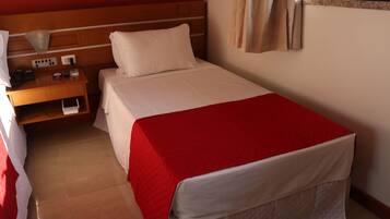 A hotel room with a single bed, a wooden nightstand with a lamp, and a window with curtains.