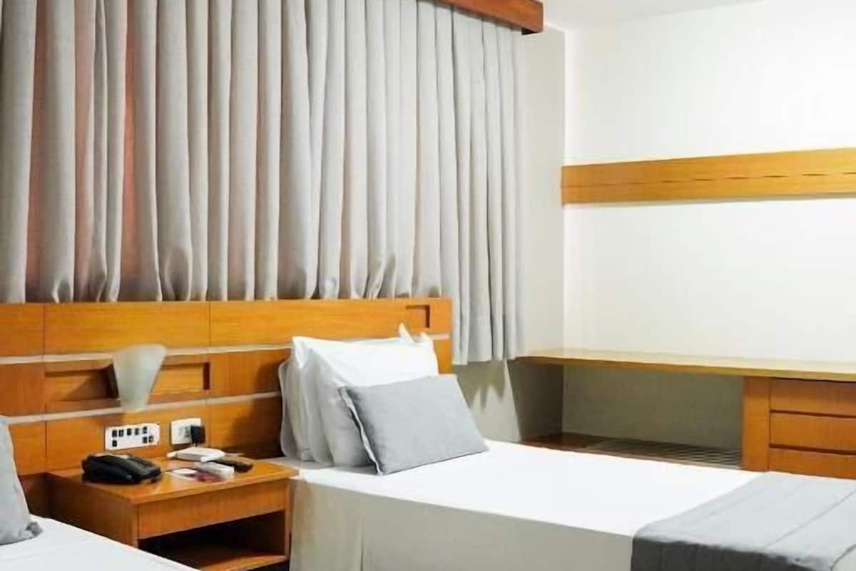 A hotel room with two beds, a wooden headboard, a desk, and a large window with curtains.