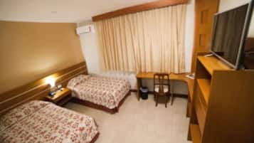 Habitación de hotel con dos camas, un escritorio, una silla, un televisor y una ventana con cortinas.