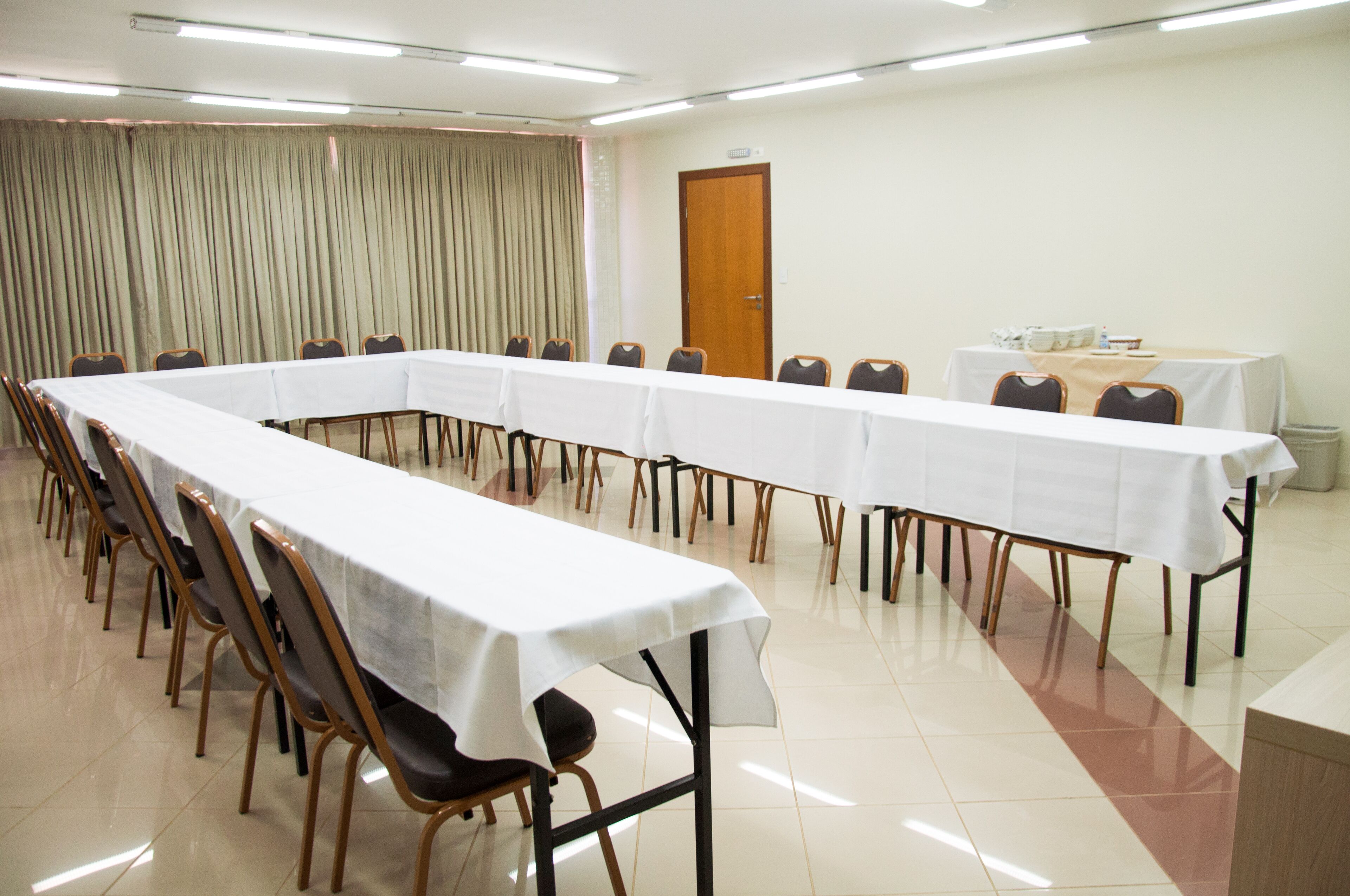 Un salón de conferencias con una larga mesa, sillas y una pequeña mesa cubierta con un mantel.