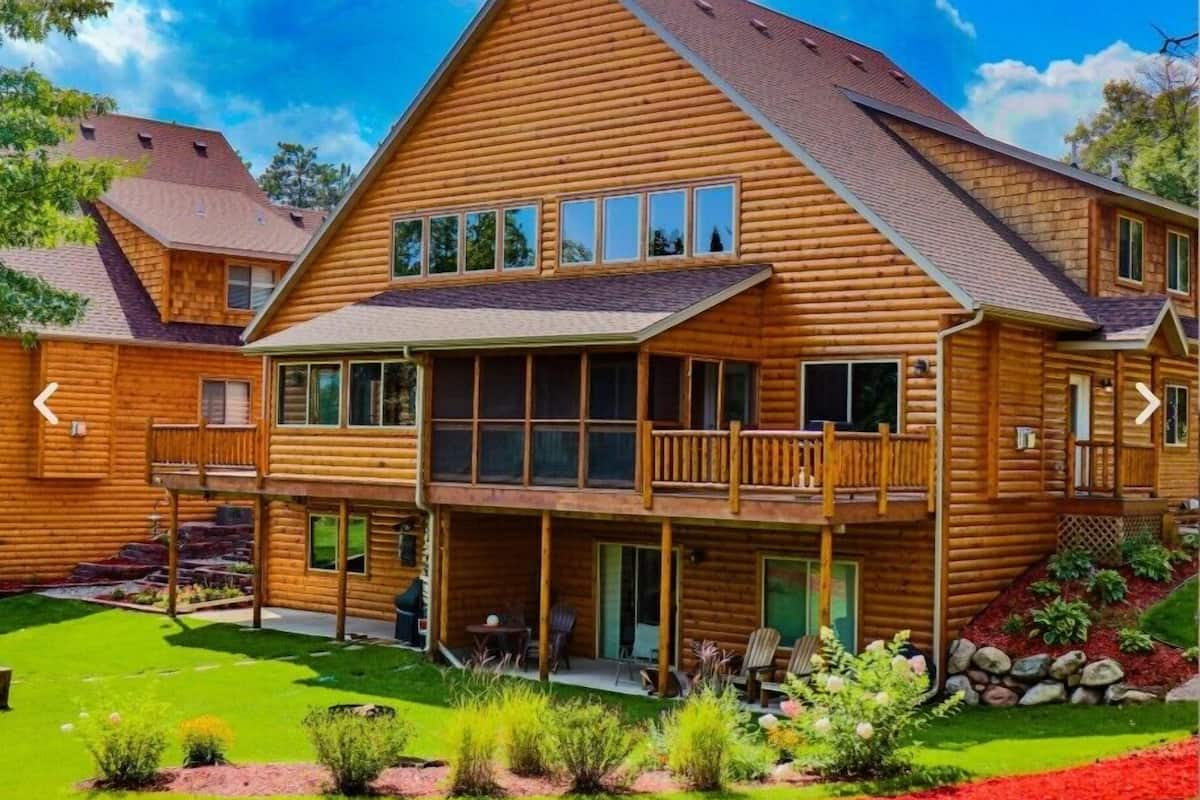 A log cabin with a large deck, multiple windows, and a well-maintained garden.