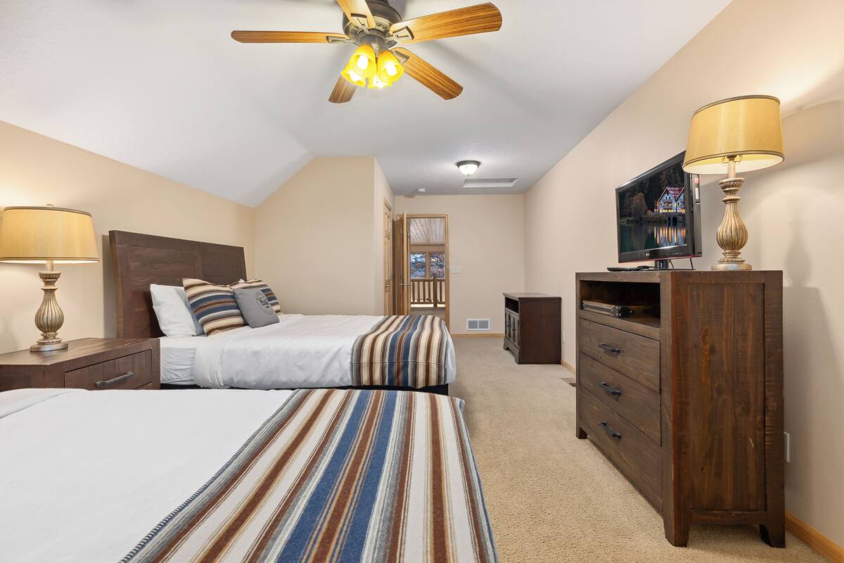 A bedroom with two beds, a ceiling fan, a TV, a dresser, and a lamp.