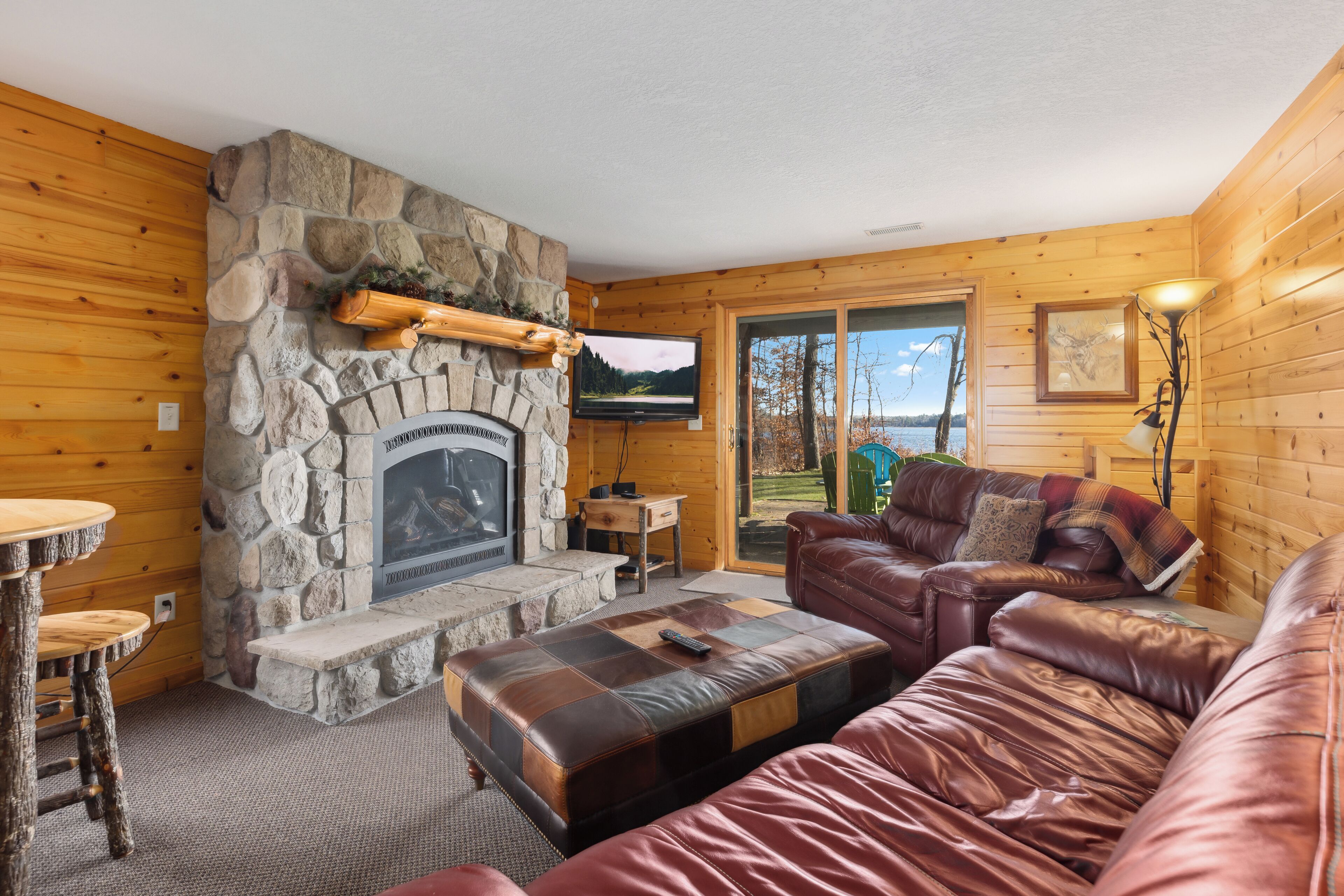A cozy cabin interior with a stone fireplace, leather sofa, and a television mounted on the wall.