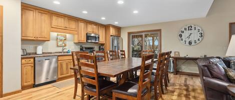 Una cocina moderna con armarios de madera, electrodomésticos de acero inoxidable y una zona de comedor con mesa y sillas de madera.