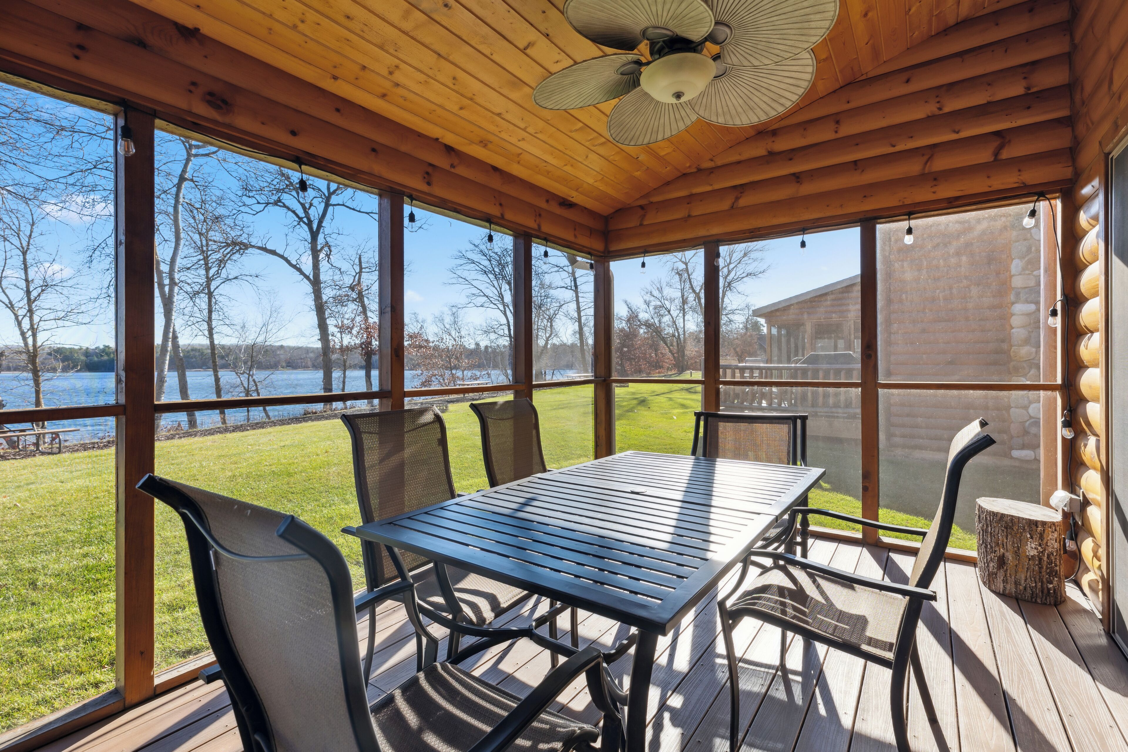 A covered patio with a table and chairs, large windows, and a view of a lake.