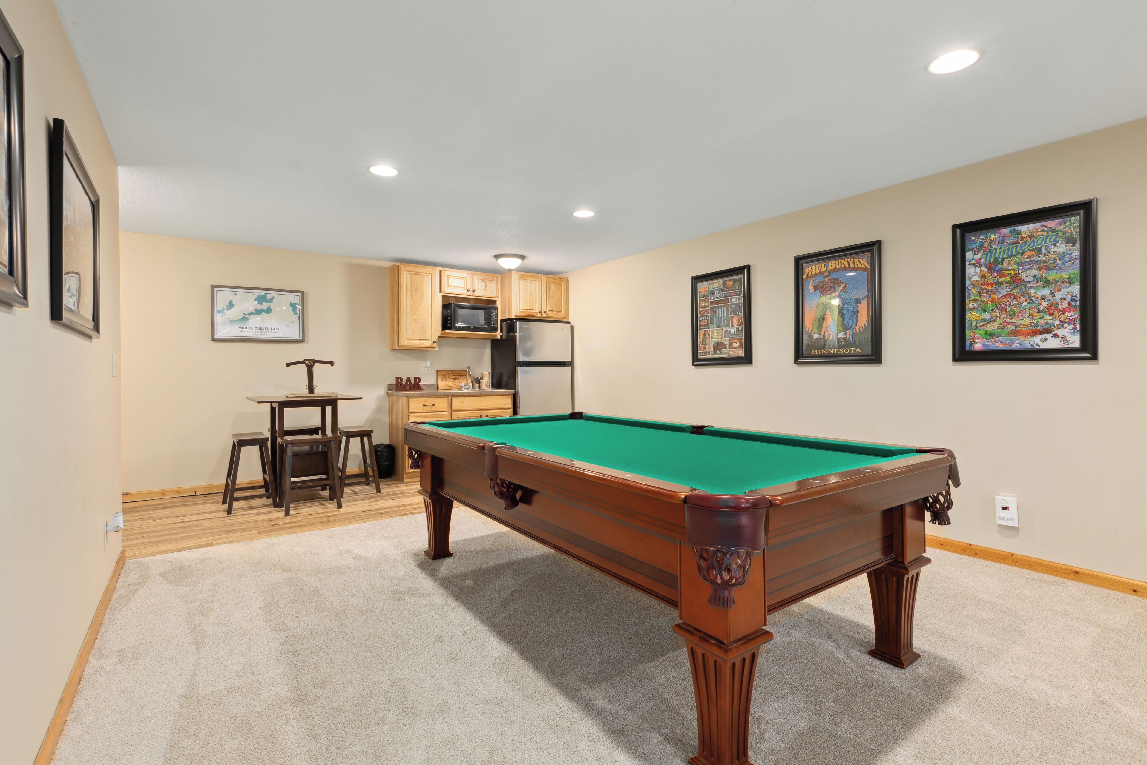 A pool table in a room with beige walls, wooden cabinets, and framed artwork.