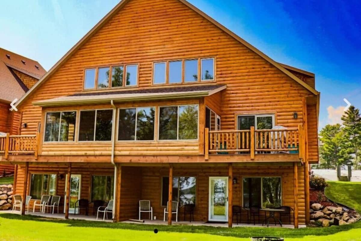 A two-story log cabin with a balcony, large windows, and outdoor seating.