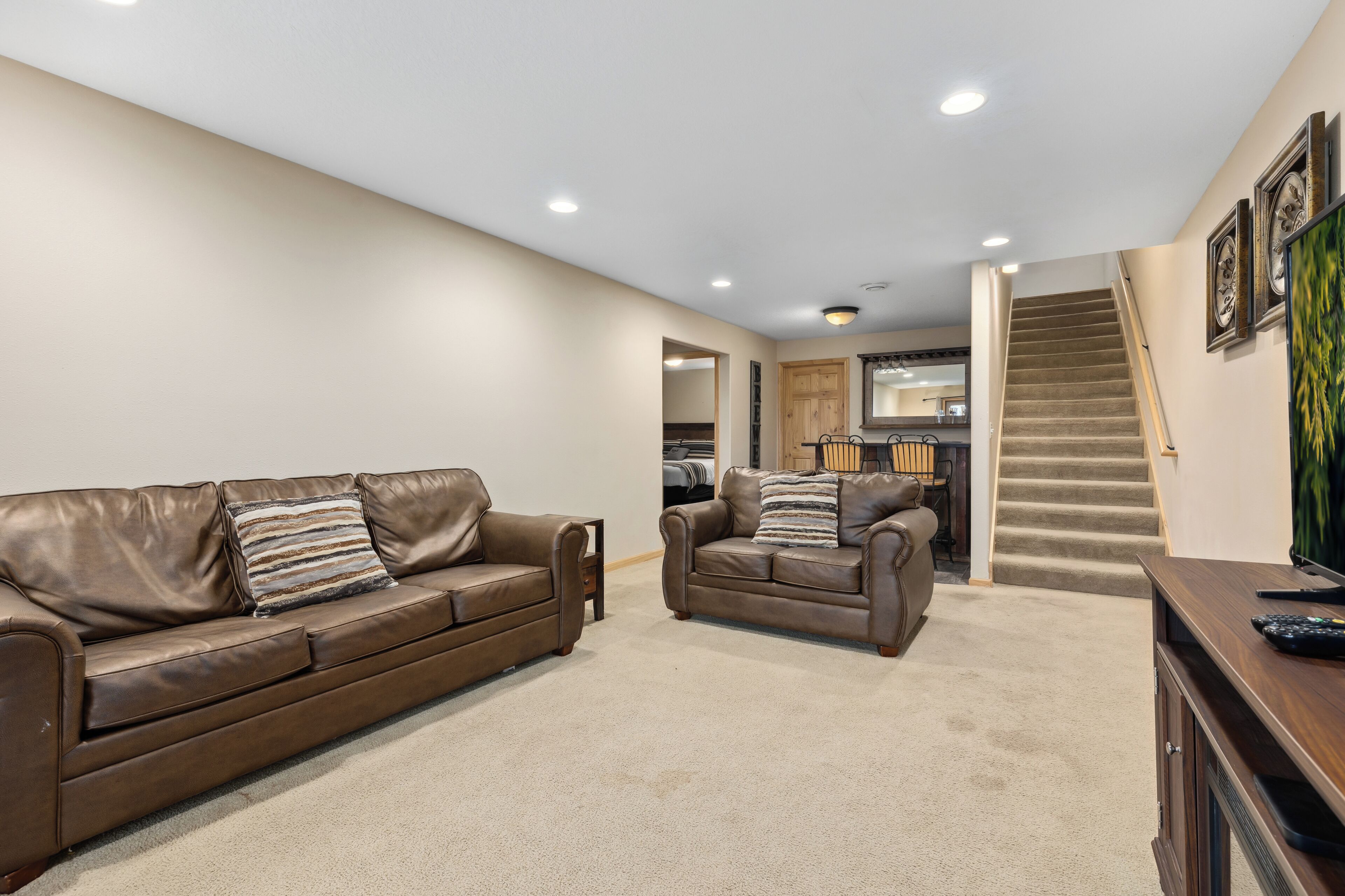 Ein geräumiges Wohnzimmer mit braunem Ledersofa und Sessel, einem Holztisch und einer Treppe, die in einen oberen Bereich führt.
