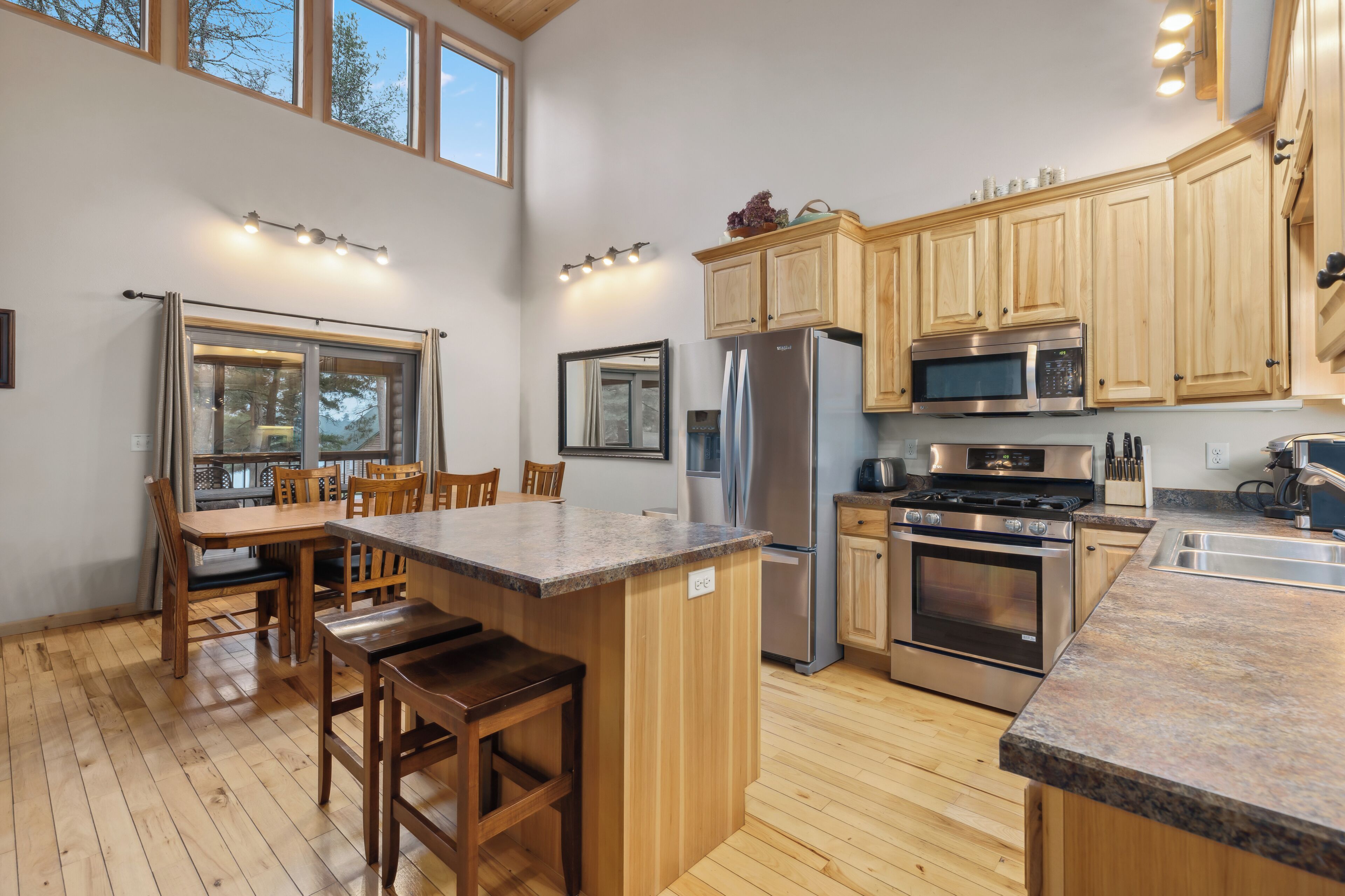 A modern kitchen with wooden cabinets, stainless steel appliances, a granite countertop, and a dining area with wooden chairs.