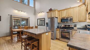 A modern kitchen with wooden cabinets, stainless steel appliances, a granite countertop, and a dining area with wooden chairs.