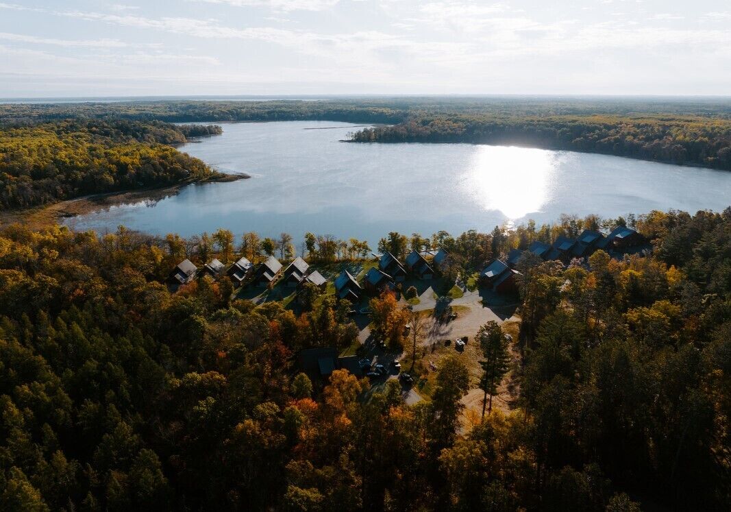 Vue aérienne d’un complexe hôtelier au bord d’un lac, composé de plusieurs chalets entourés d’une forêt dense.