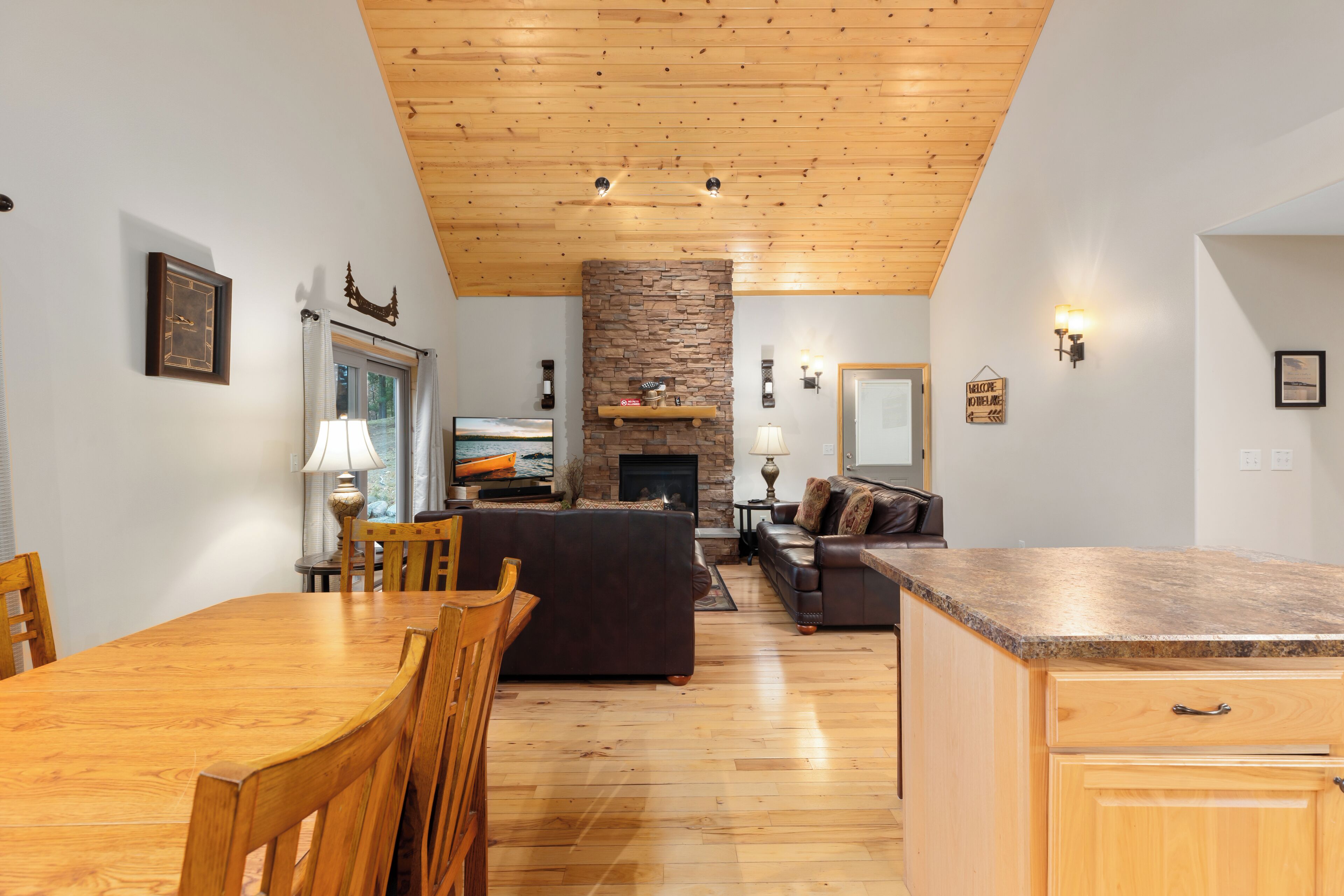 Amplia sala de estar con techo de madera, chimenea de piedra y encimera de cocina.