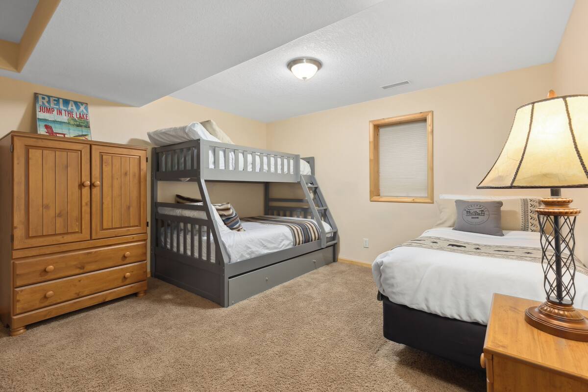 A bedroom with a bunk bed, a wooden dresser, a bedside lamp, and a framed picture on the wall.
