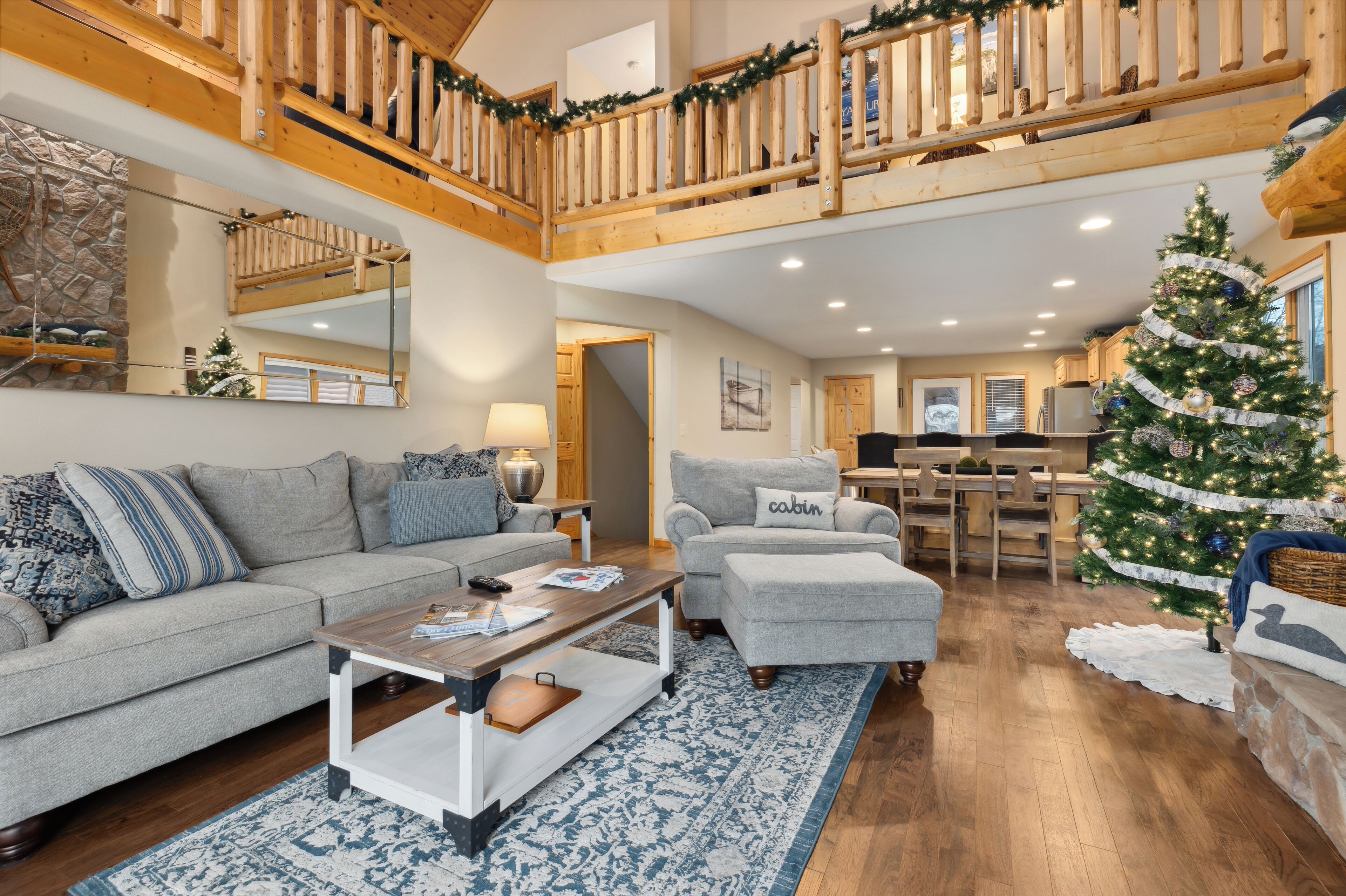 A spacious living room with a high ceiling, wooden balcony railing, and a large Christmas tree.