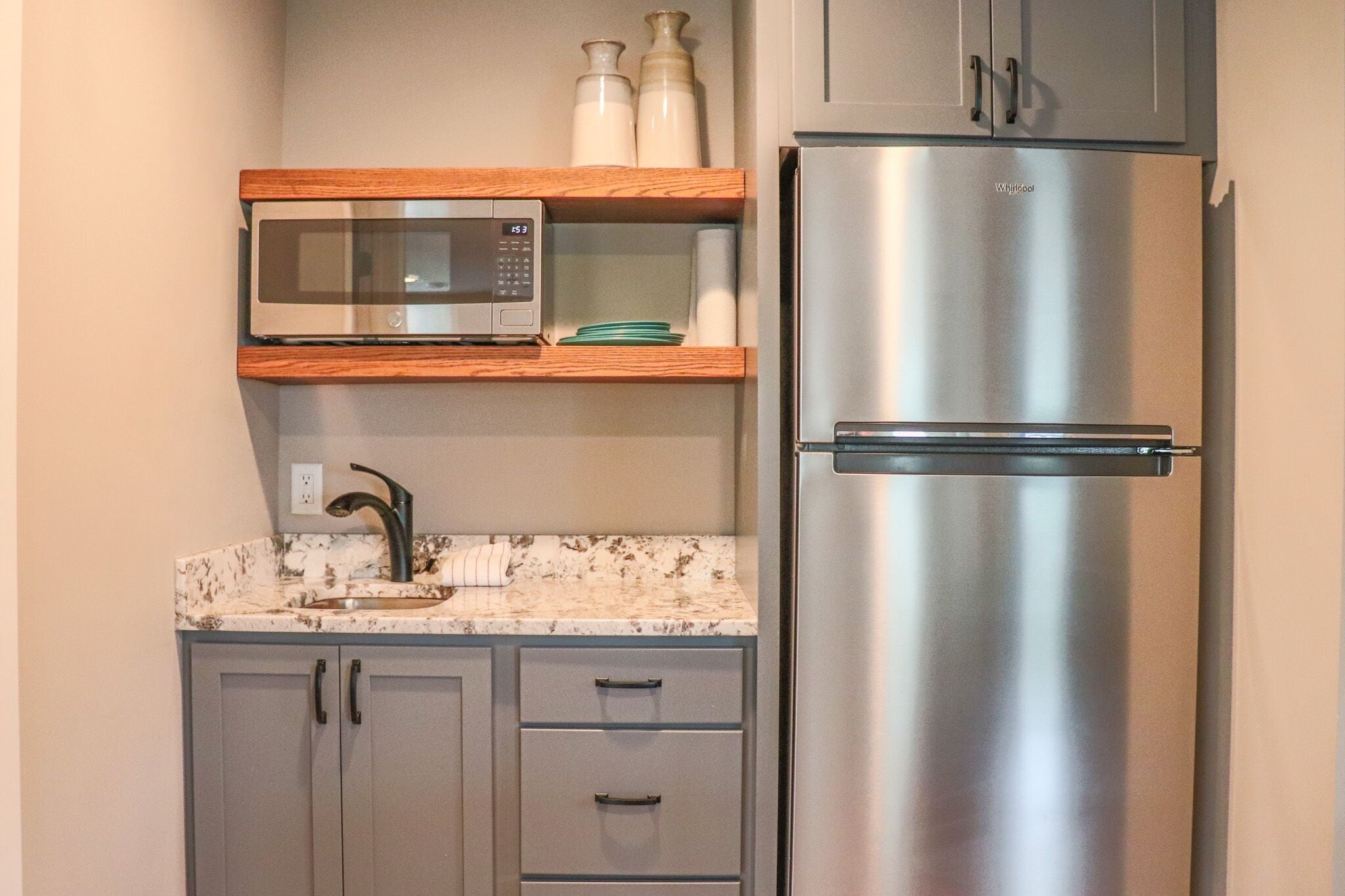A kitchen with a stainless steel refrigerator, a microwave, and a sink with a marble countertop.
