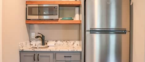 A kitchen with a stainless steel refrigerator, a microwave, and a sink with a marble countertop.