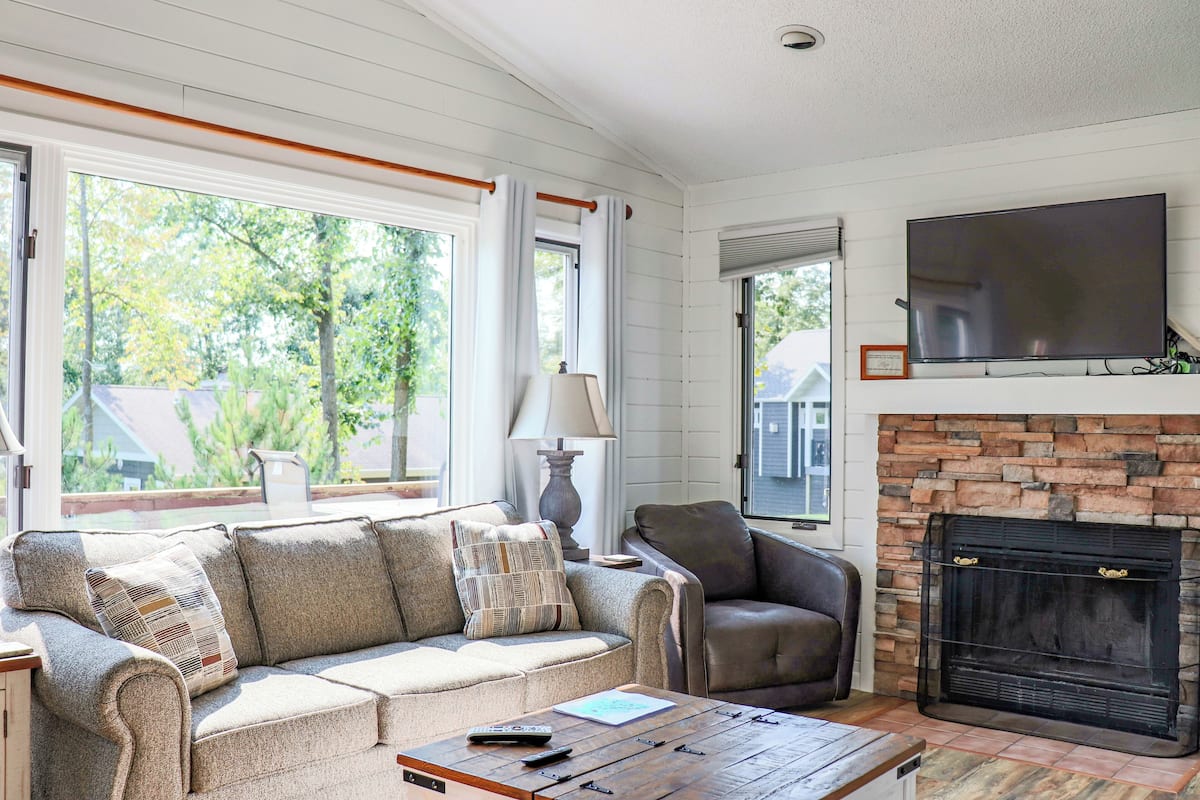 A living room with a sofa, armchair, fireplace, and a television mounted on the wall.