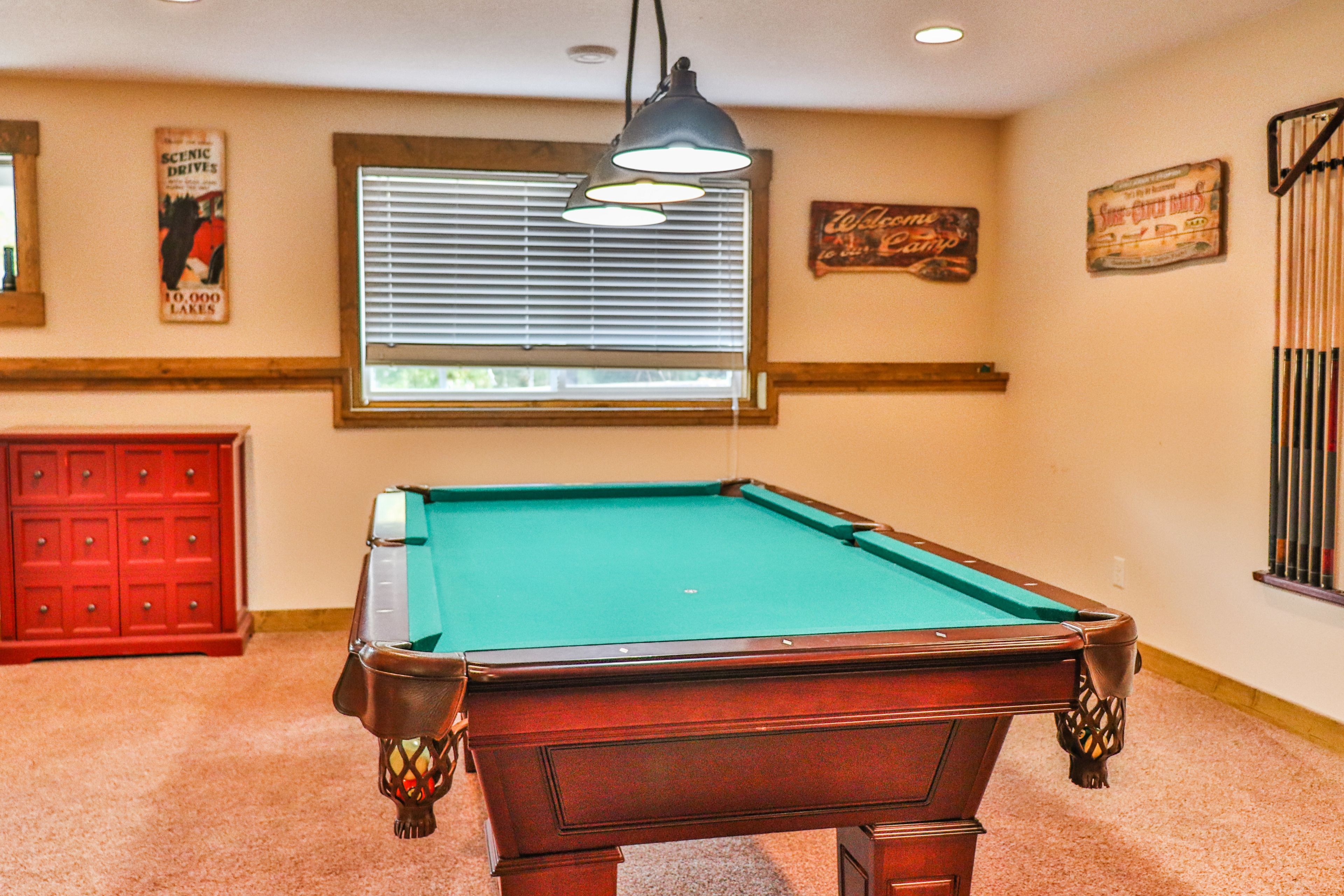A pool table with a green felt surface, a red cabinet, and a window with blinds.