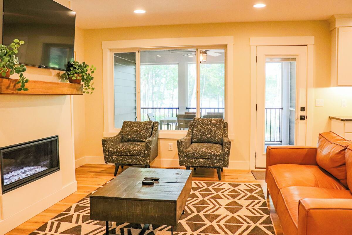 A living room with a fireplace, two patterned armchairs, a coffee table, and a leather sofa.