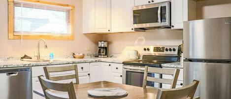 Una cocina moderna con armarios blancos, electrodomésticos de acero inoxidable y una mesa de comedor de madera.