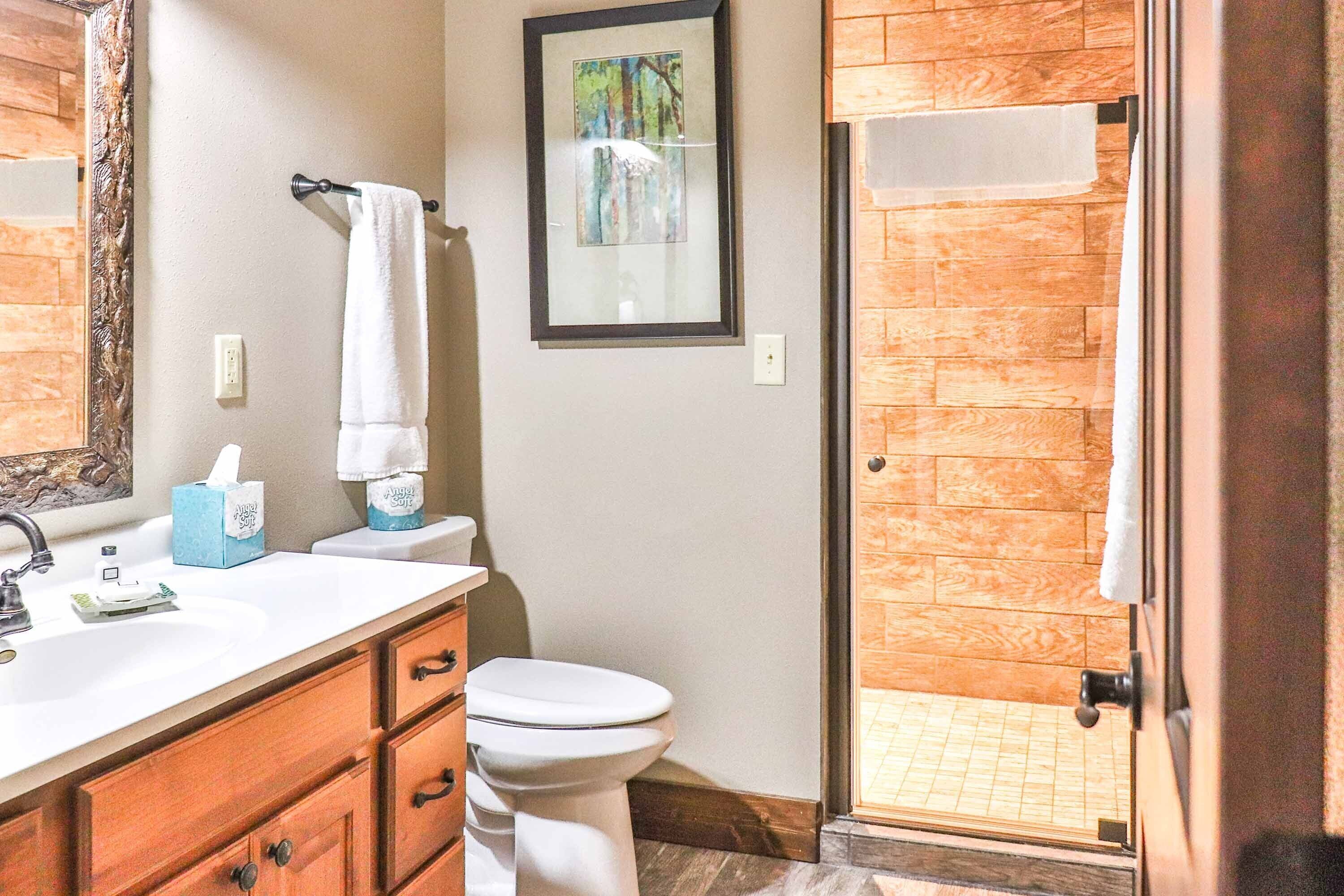 A bathroom with a wooden floor, a white sink, a toilet, and a framed picture on the wall.