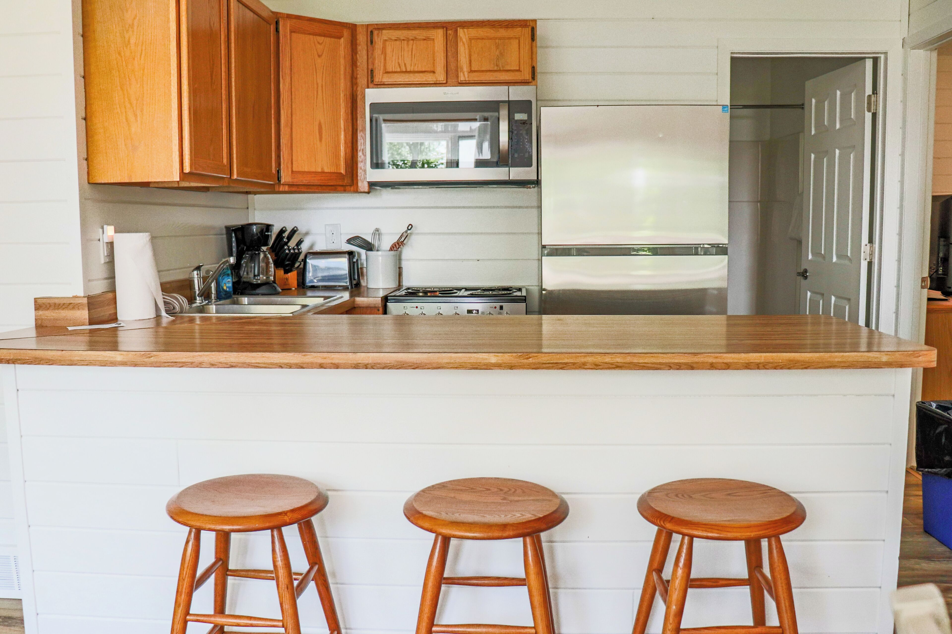 A kitchen with wooden cabinets, a microwave, a stove, and three wooden stools.