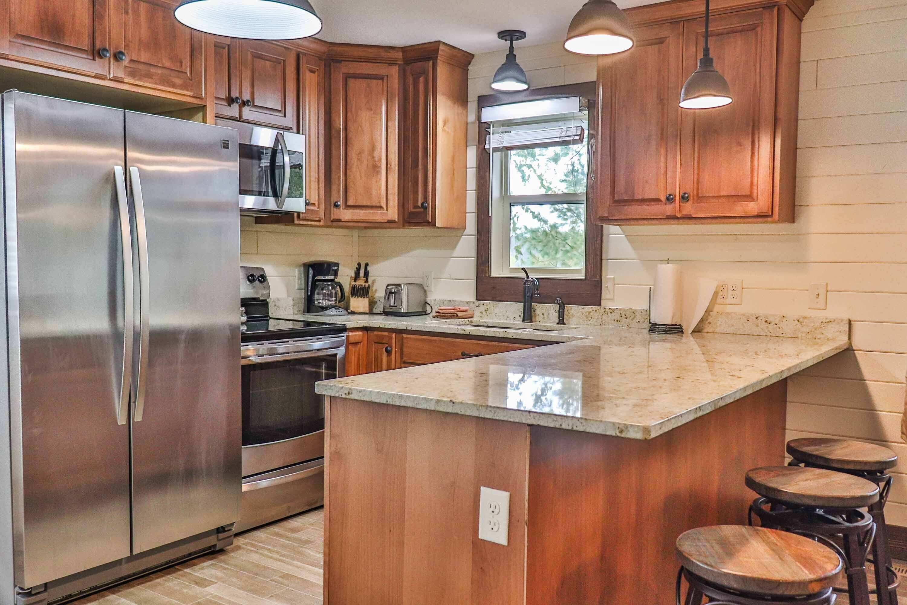 A kitchen with wooden cabinets, stainless steel appliances, a large island with stools, and pendant lighting.