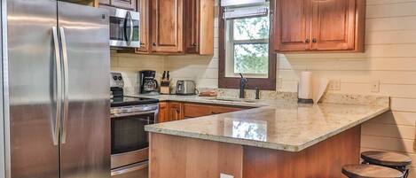 A kitchen with wooden cabinets, stainless steel appliances, a large island with stools, and pendant lighting.