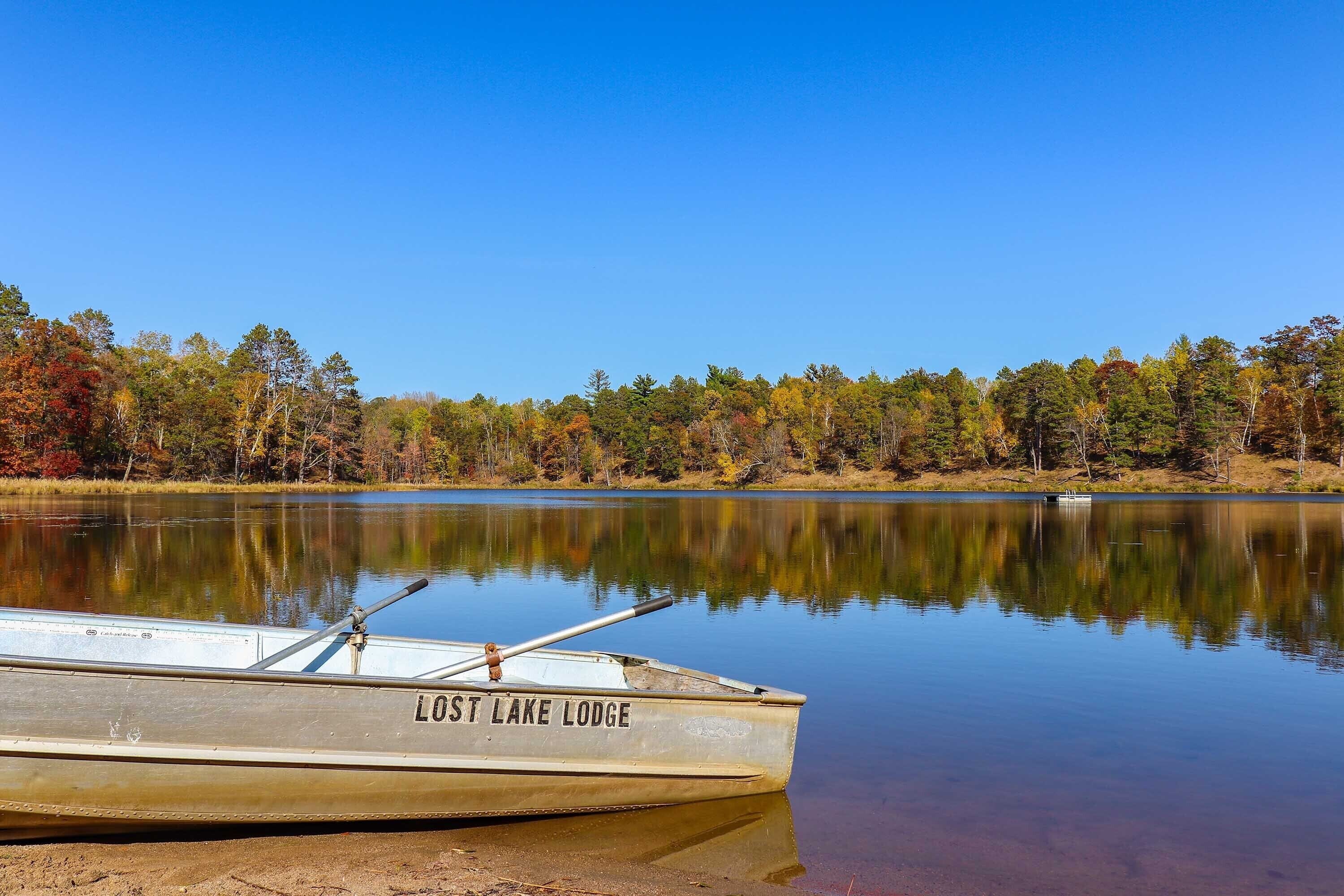 A boat named "Lost Lake Lodge" docked at a calm lake with a forested shoreline.