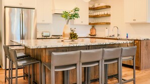 Une cuisine moderne dotée d’un grand îlot central, d’appareils électroménagers en acier inoxydable et de tabourets de bar.