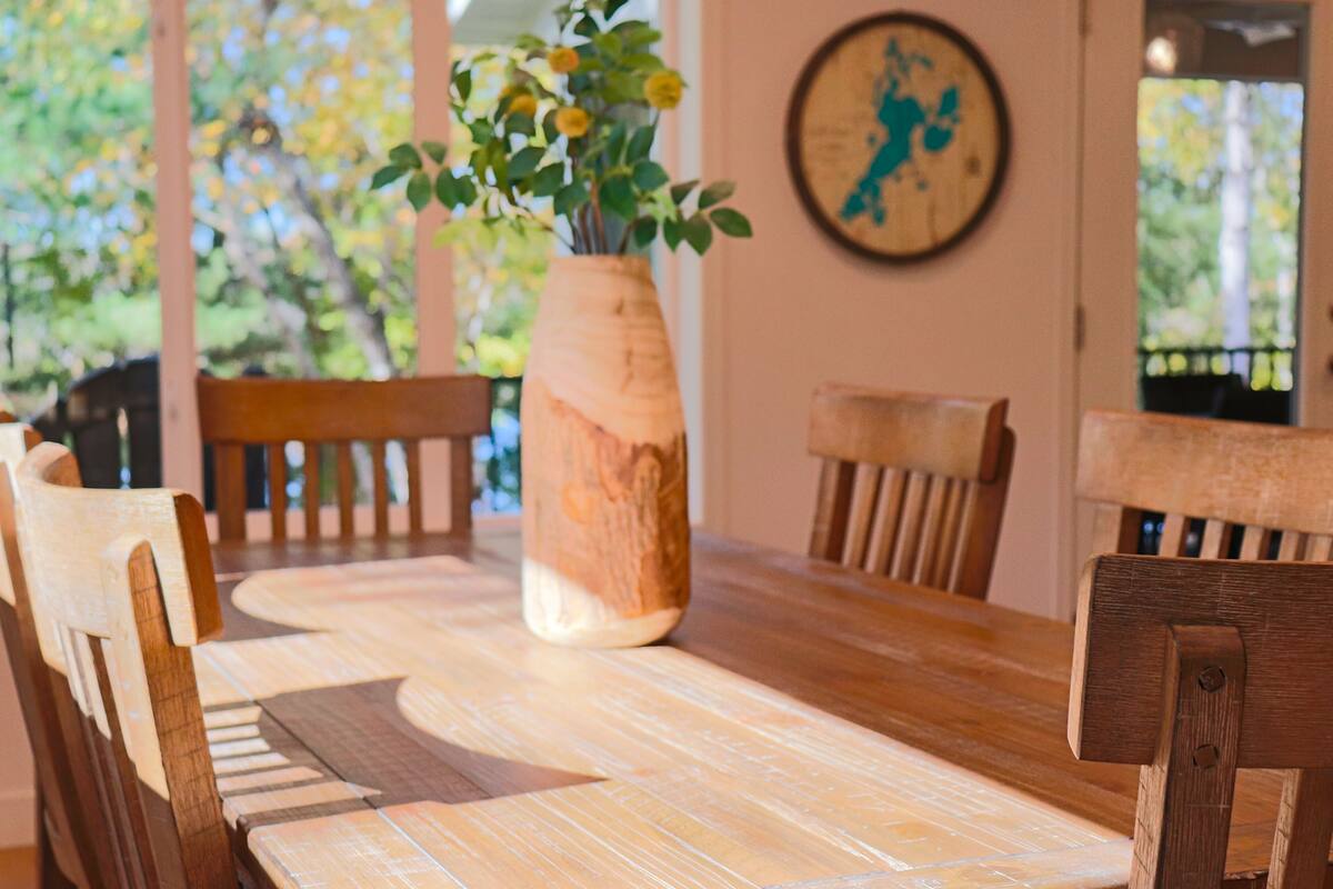 A wooden dining table with a vase of flowers, surrounded by wooden chairs.