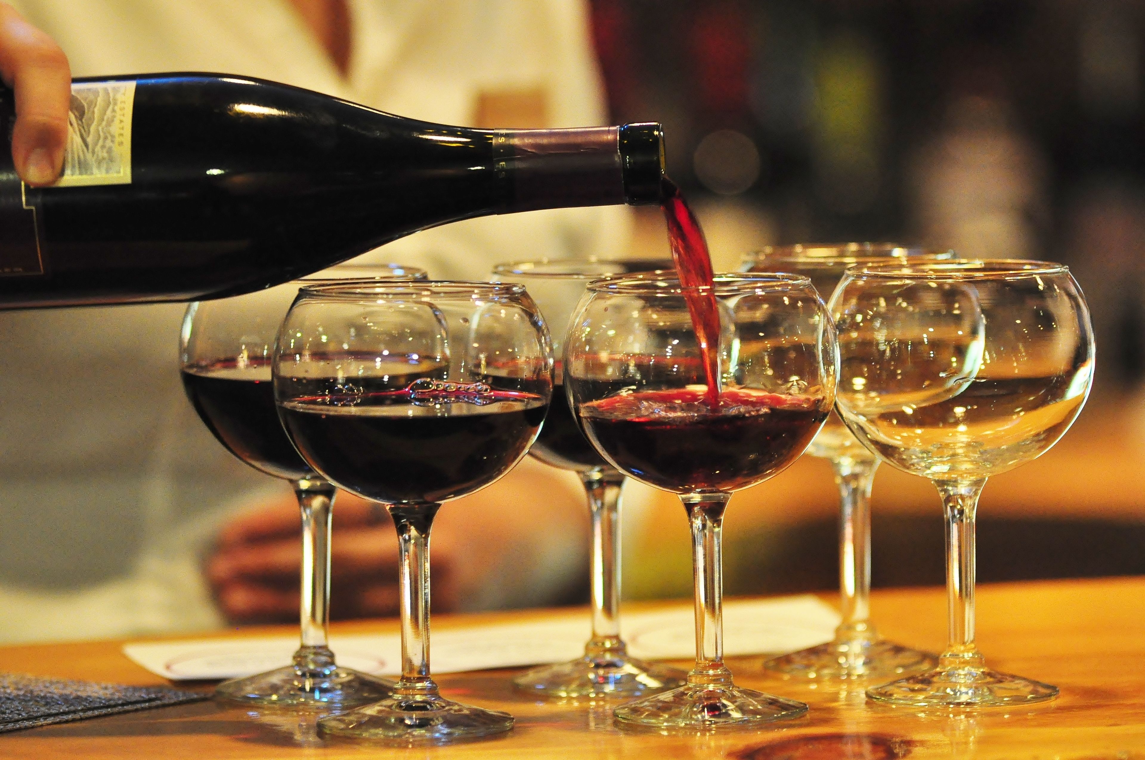 A bottle of red wine being poured into several wine glasses on a table.