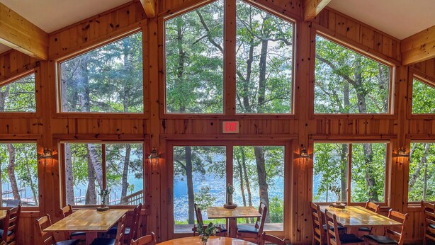 Une cabane en bois dotée de grandes fenêtres donnant sur une forêt et un lac.