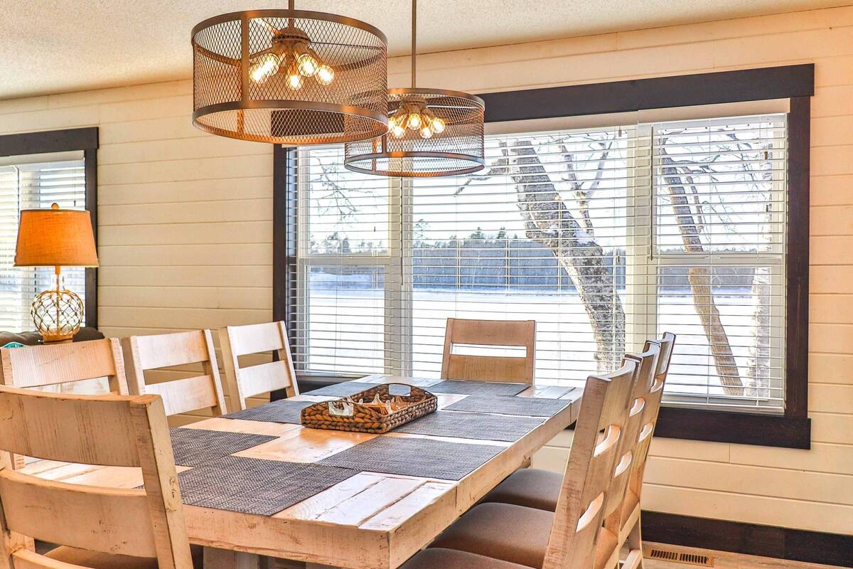 A dining area with a wooden table, chairs, and a window with a view of a staircase and trees.